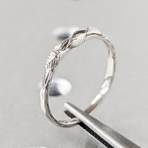 May include: A delicate silver ring with a leaf design. The ring is being held by tweezers on a gray surface with small holes.