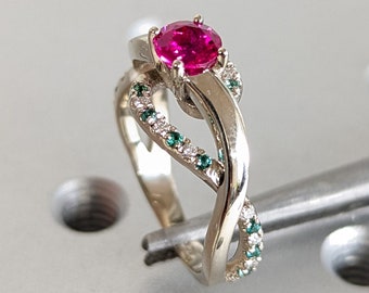 May include: A white gold ring with a pink gemstone and green gemstones set in the band.