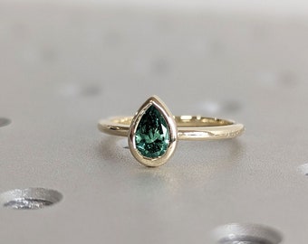 May include: A gold ring with a pear-shaped green gemstone set in a bezel setting.