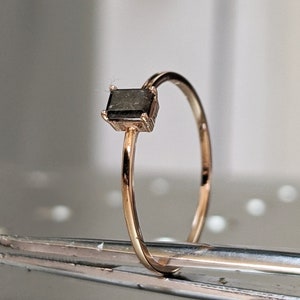 May include: A gold ring with a square, dark gray gemstone.