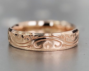 May include: Rose gold ring with an engraved floral pattern. The ring features a detailed design of swirling leaves and sunburst motifs. The band has a polished finish, reflecting light. This piece is suitable for everyday wear or special occasions.