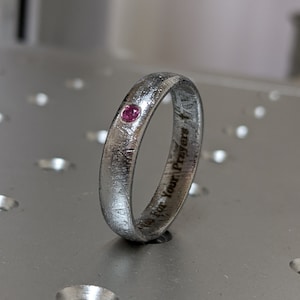 May include: A silver ring with a small pink gemstone and the inscription "This for Your Prayers" engraved on the band.