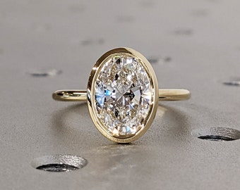 May include: A gold ring with a bezel setting featuring a large oval-shaped diamond.