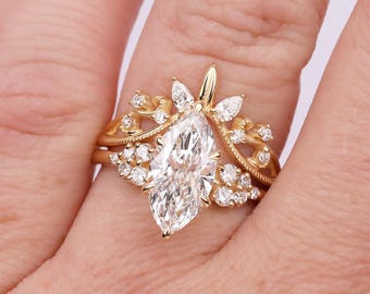 Può includere: Un set di anelli in oro con un diamante centrale taglio marquise circondato da diamanti più piccoli taglio rotondo. La fascia presenta un design curvo e intricato con dettagli milgrain, creando un aspetto stratificato con la pietra marquise come punto focale.