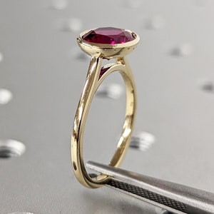Puede incluir: Un anillo de oro con engaste de bisel que presenta una piedra preciosa de color rojo intenso.