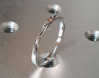 May include: A simple silver band ring with a slightly rounded edge. The ring is sitting on a silver surface with multiple holes.