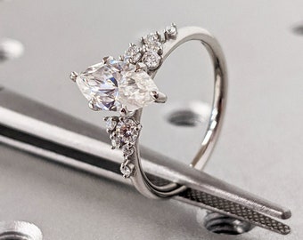 Op de afbeelding: Een zilveren ring met een grote marquise-vormige diamant en kleinere diamanten gezet in een delicate, gebogen band.
