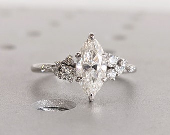 Op de afbeelding: Een verlovingsring met een peervormige diamant en een delicate, bloemige setting. De ring heeft een grote middelste steen en kleinere accentdiamanten op de band.