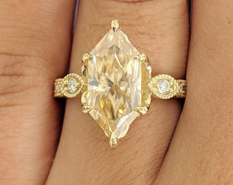 May include: A gold ring featuring a large, light yellow, hexagonal-cut gemstone. The ring has a detailed, textured band with small, round accent stones on each side of the main stone. The ring is set in a gold band.