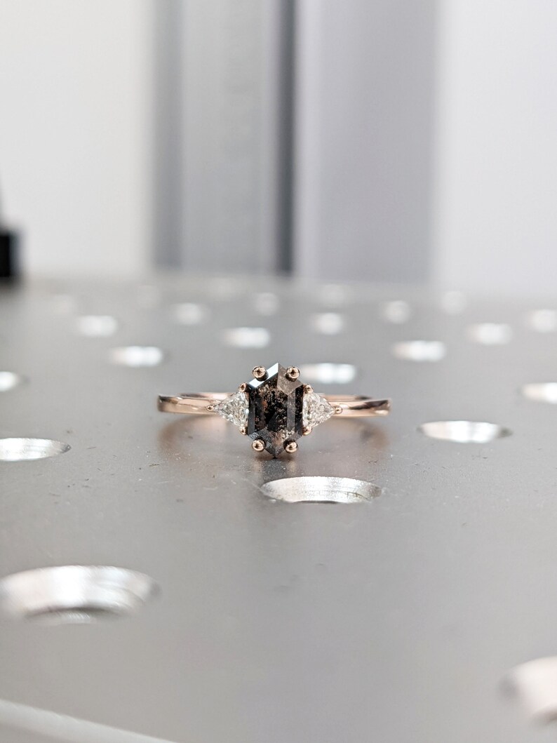 May include: A rose gold engagement ring with a gray octagon-shaped diamond and two smaller triangular diamonds on either side.
