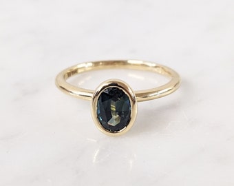 May include: A gold ring with a dark blue oval gemstone set in a bezel setting.