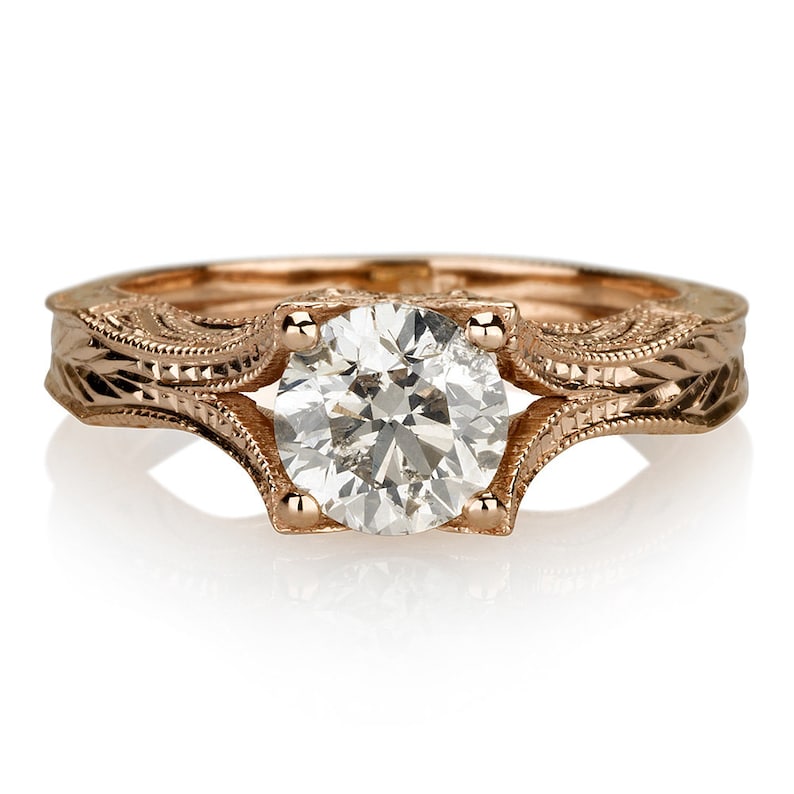 K&ouml;nnte beinhalten: Ein Verlobungsring aus Ros&eacute;gold mit einem runden Brillanten, der in einer Vintage-Fassung gefasst ist. Die Ringschiene ist mit filigranen Schn&ouml;rkeln und Milgrain-Details verziert.