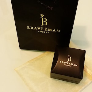 以下が含まれることがあります： 「Braverman Jewelry」と金色で書かれたロゴが付いた黒いギフトバッグと、「Braverman Jewelry」と金色で書かれたロゴが付いた小さな黒いジュエリーボックスです。