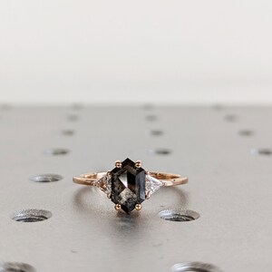 May include: A rose gold ring with a black octagonal diamond and two smaller diamonds on the side.