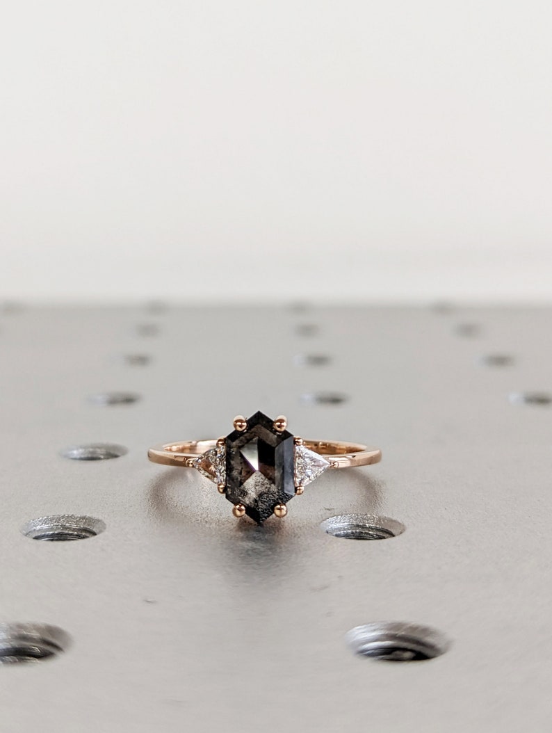 May include: A rose gold ring with a black octagonal diamond and two smaller diamonds on the side.