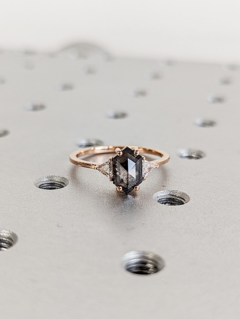 May include: A rose gold ring with a hexagonal black diamond and two smaller triangular diamonds on either side.