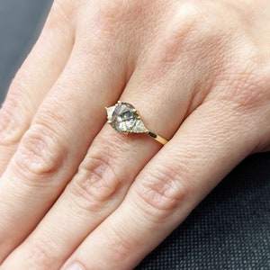 Puede incluir: Un anillo de oro con una piedra ovalada gris y dos piedras triangulares m&aacute;s peque&ntilde;as a cada lado.