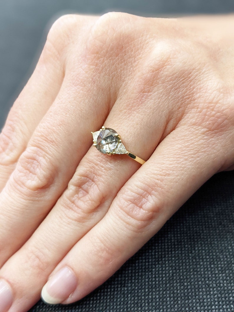 Puede incluir: Un anillo de oro con una piedra ovalada gris y dos piedras triangulares m&aacute;s peque&ntilde;as a cada lado.