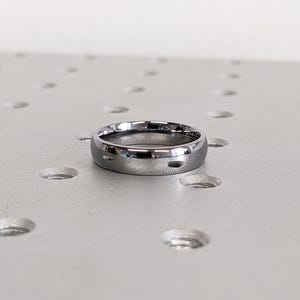 May include: A polished, silver-colored ring with a rounded band. The ring has a smooth, reflective surface and a simple, minimalist design. The ring is likely made of metal and is suitable for everyday wear. The ring is approximately 0.25 inches wide.