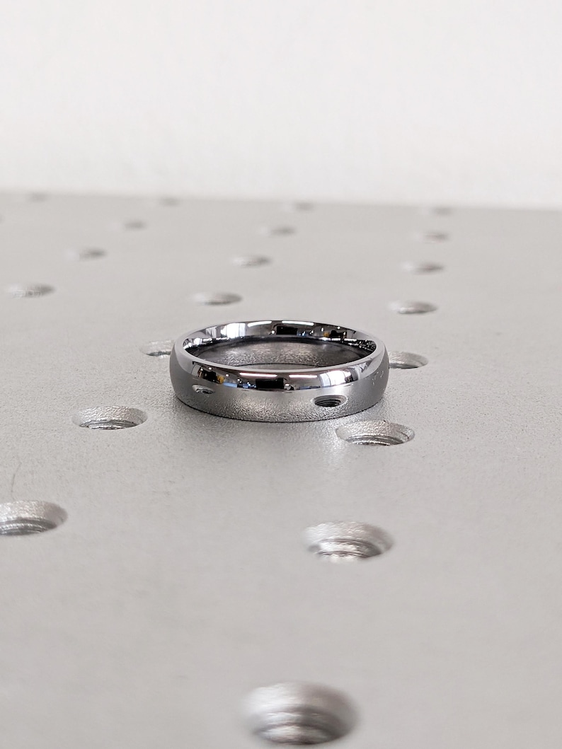 May include: A polished, silver-colored ring with a rounded band. The ring has a smooth, reflective surface and a simple, minimalist design. The ring is likely made of metal and is suitable for everyday wear. The ring is approximately 0.25 inches wide.