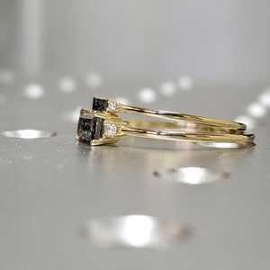 May include: Two gold rings with a black square gemstone and small clear gemstones on the band. The rings are stacked on top of each other.