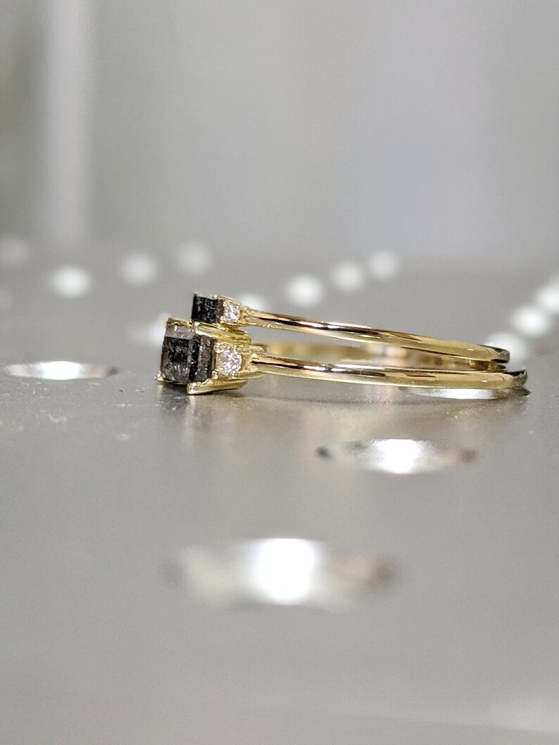 May include: Two gold rings with a black square gemstone and small clear gemstones on the band. The rings are stacked on top of each other.