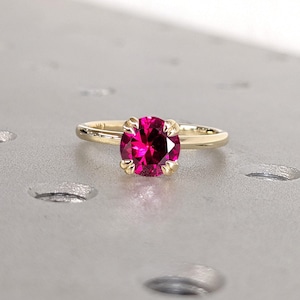 May include: A gold ring with a bright pink oval gemstone set in a four-prong setting.