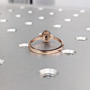 May include: A rose gold ring with a black oval-shaped gemstone surrounded by smaller clear gemstones.