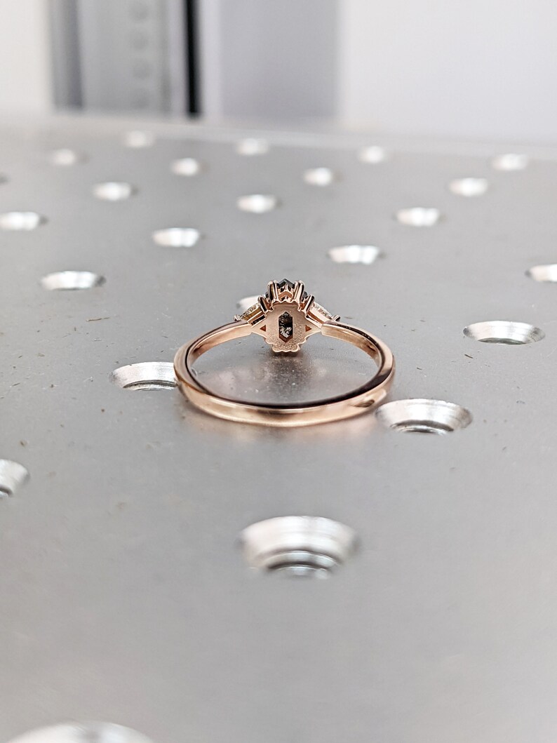 May include: A rose gold ring with a black oval-shaped gemstone surrounded by smaller clear gemstones.