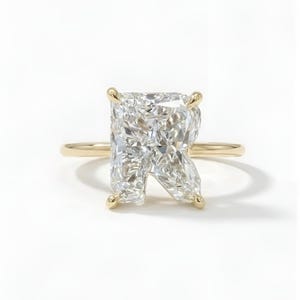 Pode incluir: Anel de ouro com um grande diamante de corte radiante. O diamante transparente é fixado por quatro garras. O anel tem uma banda de ouro simples. Apresentado sobre um fundo branco. Uma joia clássica.