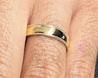 May include: A gold wedding band with a beaded edge detail. The ring is a classic design, with a polished finish. The band is approximately 3mm wide.