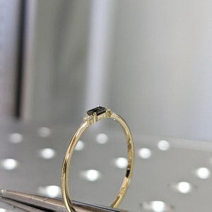 May include: A delicate gold band ring with a small black rectangular gemstone and two smaller white gemstones on either side.