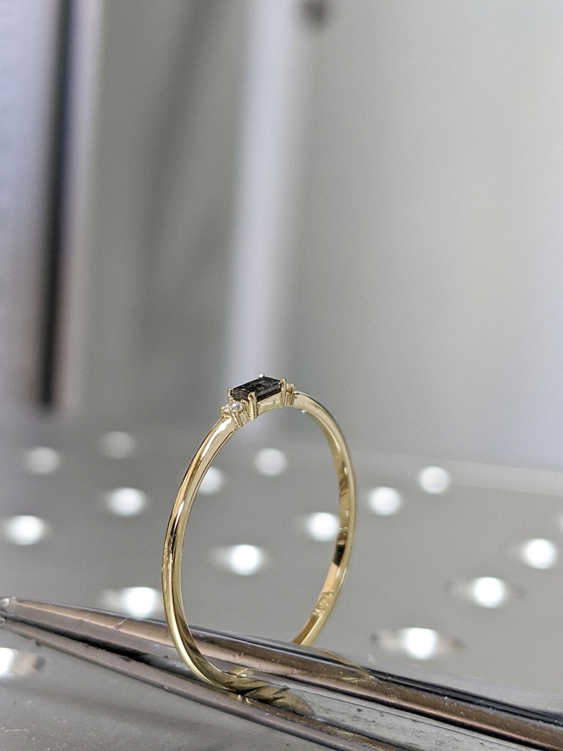May include: A delicate gold band ring with a small black rectangular gemstone and two smaller white gemstones on either side.