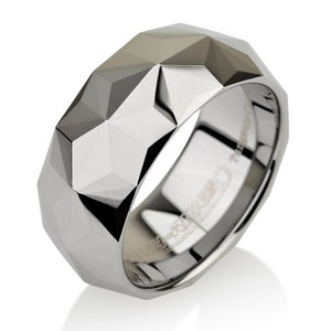 May include: A silver ring with a geometric, faceted design. The ring has a wide band and a polished, reflective surface. The facets create a play of light and shadow, giving the ring a modern, architectural look. The ring is likely made of a durable metal.