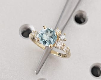 May include: A gold ring with a light blue gemstone surrounded by smaller white gemstones.