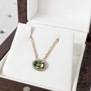 May include: A gold chain necklace with a green oval gemstone surrounded by a halo of smaller diamonds. The necklace is displayed in a wooden box with the name "BRAVERMAN" on the lid.
