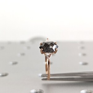 May include: A rose gold engagement ring with a black octagon-shaped diamond and two smaller triangular diamonds on either side.