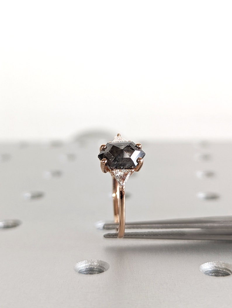 May include: A rose gold engagement ring with a black octagon-shaped diamond and two smaller triangular diamonds on either side.