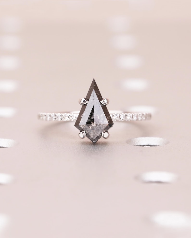 Puede incluir: Un anillo de compromiso de plata con un diamante en forma de cometa, sal y pimienta. La banda est&aacute; adornada con peque&ntilde;os diamantes brillantes. El dise&ntilde;o &uacute;nico y la piedra central oscura del anillo crean un contraste llamativo.