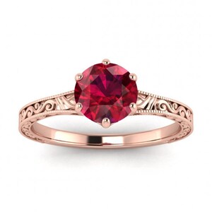 May include: A rose gold engagement ring featuring a red ruby gemstone set in a vintage-inspired filigree band.