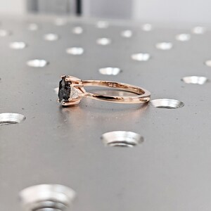May include: A rose gold engagement ring with a black oval-shaped center stone and two smaller white accent stones.