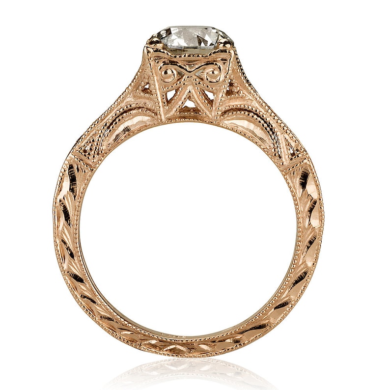 K&ouml;nnte beinhalten: Ein Verlobungsring aus Ros&eacute;gold mit einem runden Diamanten, der in einer filigranen Fassung sitzt. Die Ringschiene ist mit aufwendigen Gravuren verziert.