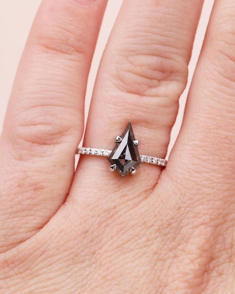 Puede incluir: Un anillo de plata con una gema gris oscura en forma de cometa. La banda est&aacute; adornada con peque&ntilde;as piedras claras. El anillo se muestra en un dedo, destacando su dise&ntilde;o y brillo.