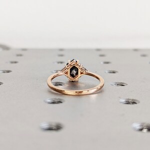 May include: A rose gold ring with a hexagonal shaped black diamond center stone and smaller diamonds on the band.