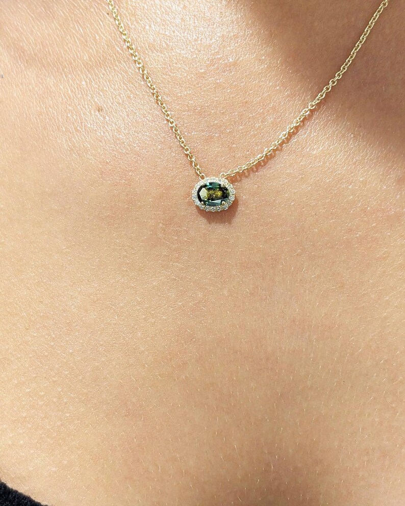 May include: A gold chain necklace with a green oval gemstone pendant surrounded by a halo of smaller diamonds.
