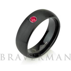 Op de afbeelding: Een zwarte ring met een geborstelde afwerking voorzien van een enkele ronde, gefacetteerde rode edelsteen in de band. De binnenzijde van de ring toont de tekst BRAVERMAN TUNGSTEN 8.5, wat het merk, materiaal en de maat van het sieraad aangeeft.