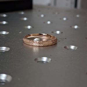 K&ouml;nnte beinhalten: Ein ros&eacute;goldener Ehering mit einem zarten Blattmotiv, das um die gesamte Band graviert ist.