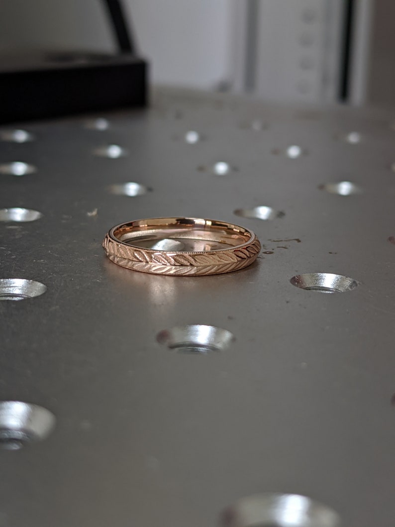 K&ouml;nnte beinhalten: Ein ros&eacute;goldener Ehering mit einem zarten Blattmotiv, das um die gesamte Band graviert ist.
