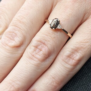 May include: A rose gold ring with a hexagonal brown diamond and two smaller triangular diamonds on the band.