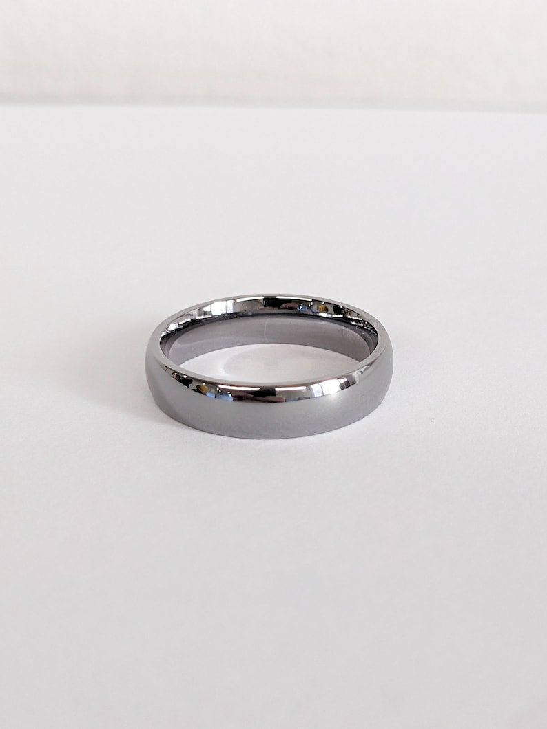 May include: A polished, gray ring with a rounded profile. The ring has a smooth, reflective surface, and is set against a white background. The ring's design is simple and elegant, suitable for everyday wear.